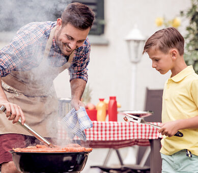 Leisure,food,people and holidays concept-man cooking meat on barbecue grill with his son,for his family at summer outdoor party.