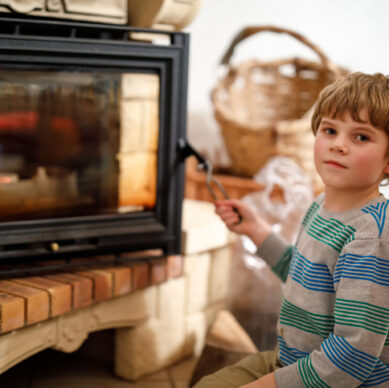 Little cute kid boy sitting by fireplace at home and helping with watching out for fire. Blond child learning to make fire. Safe handling for kids.