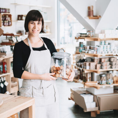 Small local business owner. Seller assistant with glass jar of pastries in interior of zero waste shop.