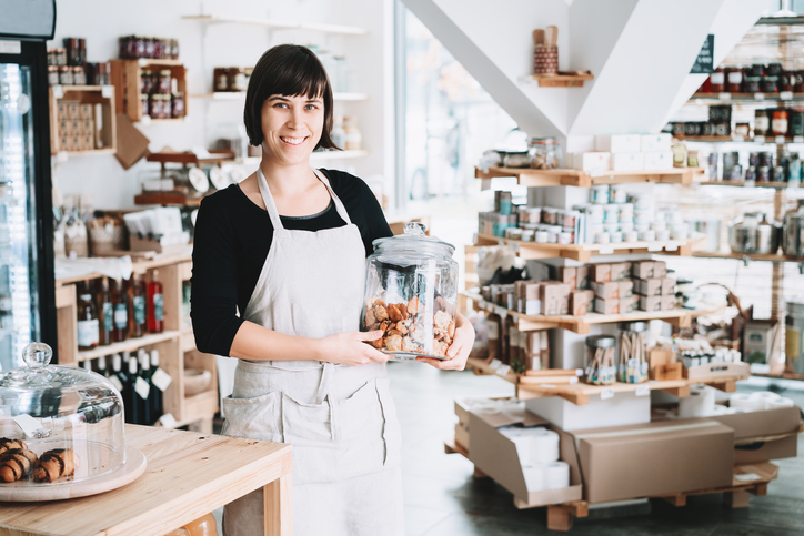 Small local business owner. Seller assistant with glass jar of pastries in interior of zero waste shop.